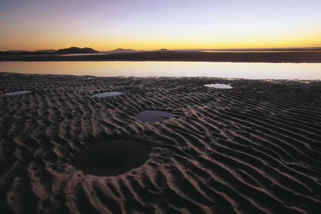 Sunset reflecting over tidal pools and rippled sand flats on a remote beach in Cape York, Australia